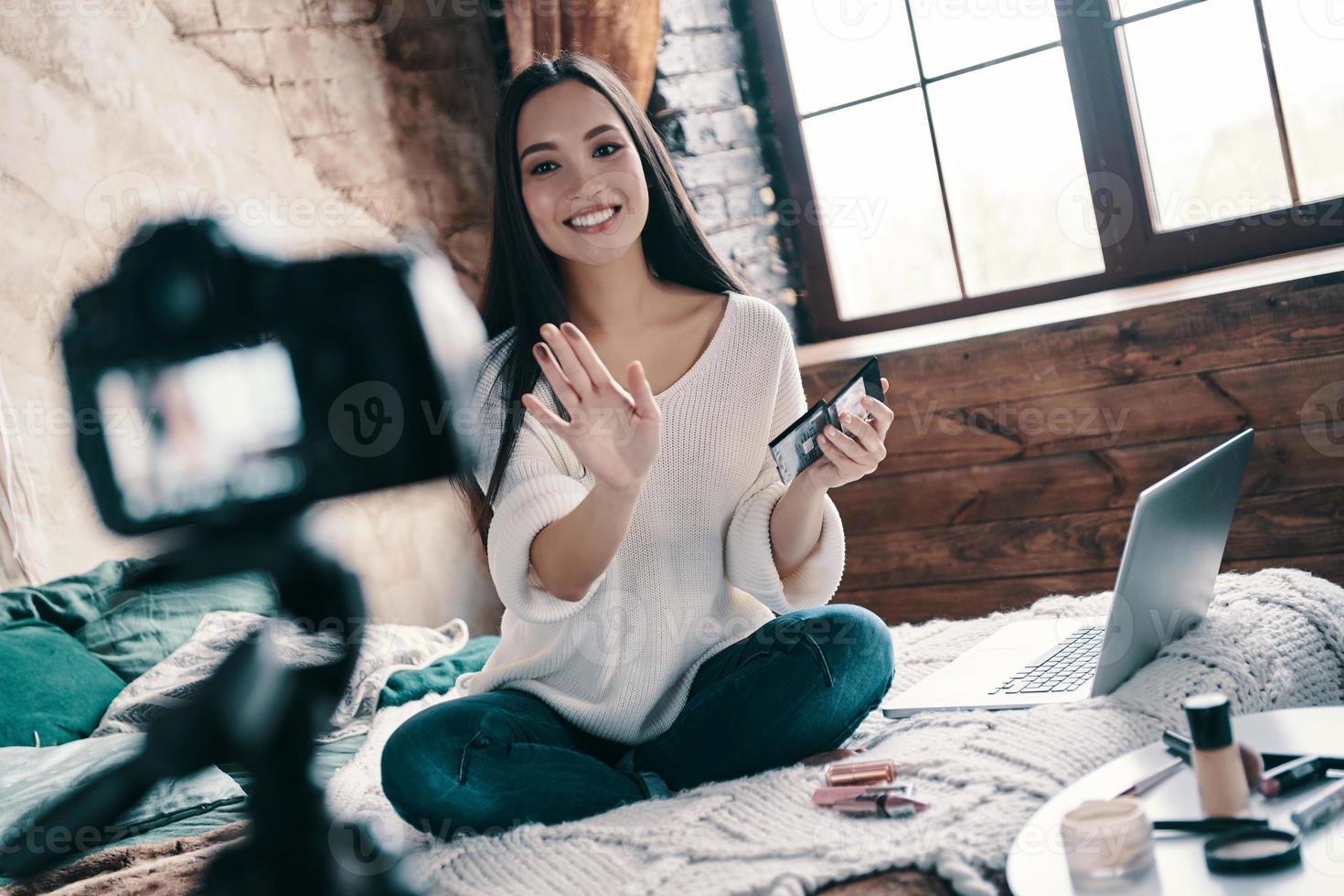 moderno influencer. bellissimo giovane donna analisi ombretti e sorridente mentre fabbricazione sociale media video foto