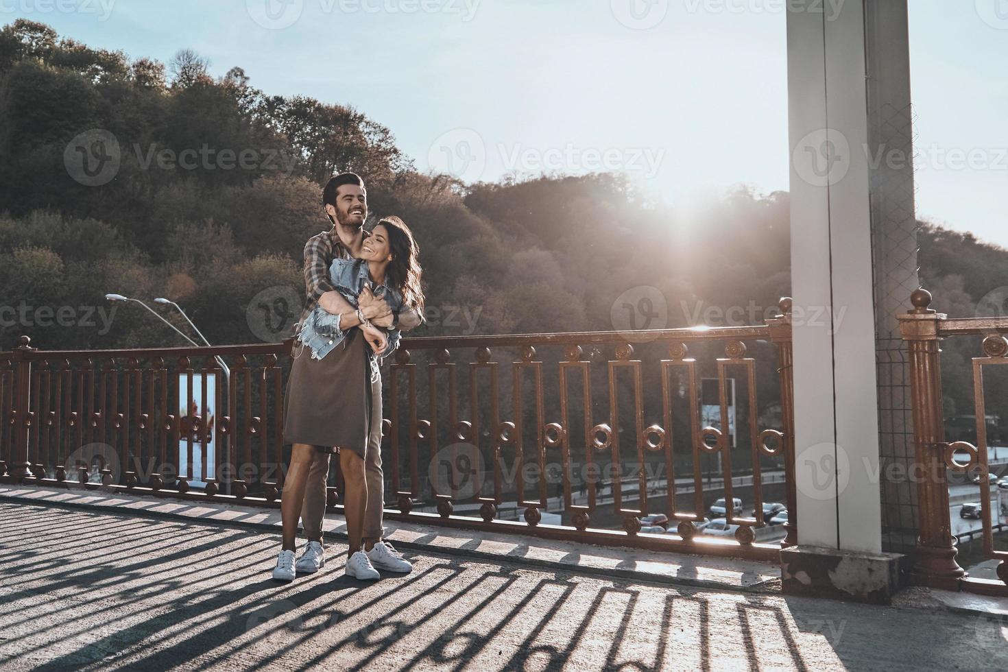 contento per essere insieme. pieno lunghezza di bellissimo bello uomo Abbracciare una persona giovane attraente donna mentre in piedi su il ponte all'aperto foto