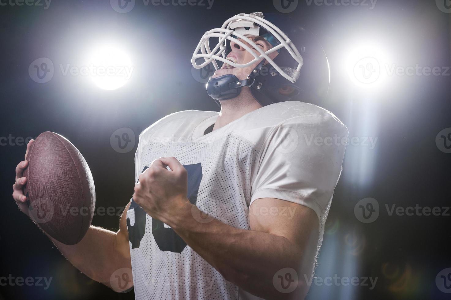 Usato per vincita. ritratto di americano calcio giocatore Tenere palla e urlando mentre in piedi contro luci foto