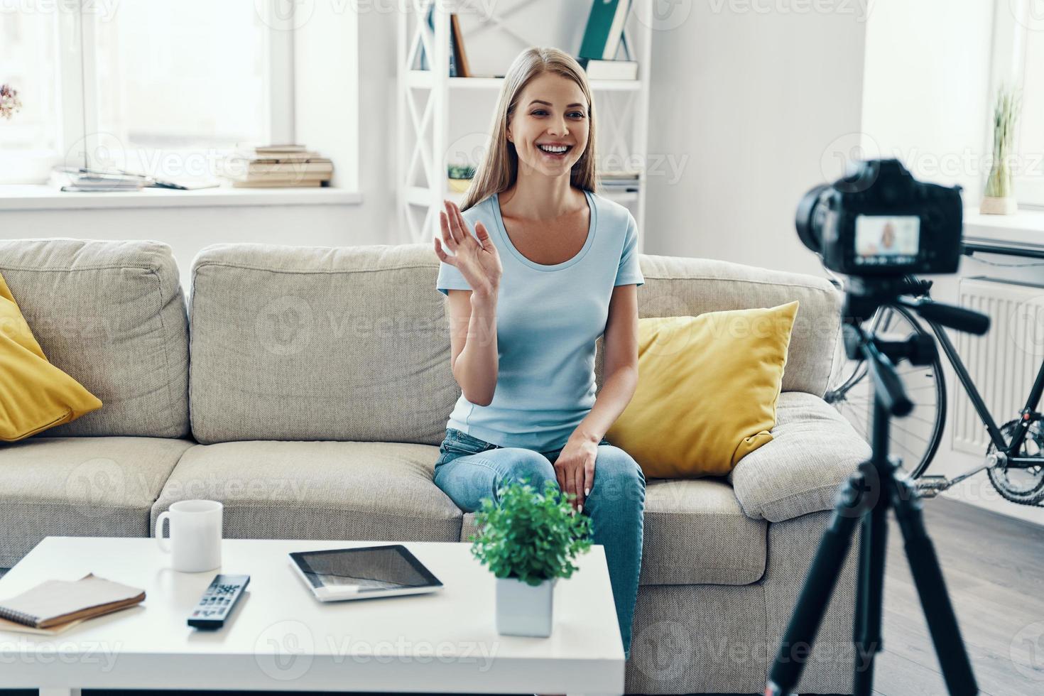 bellissimo giovane donna sorridente e agitando mentre fabbricazione sociale media video a casa foto