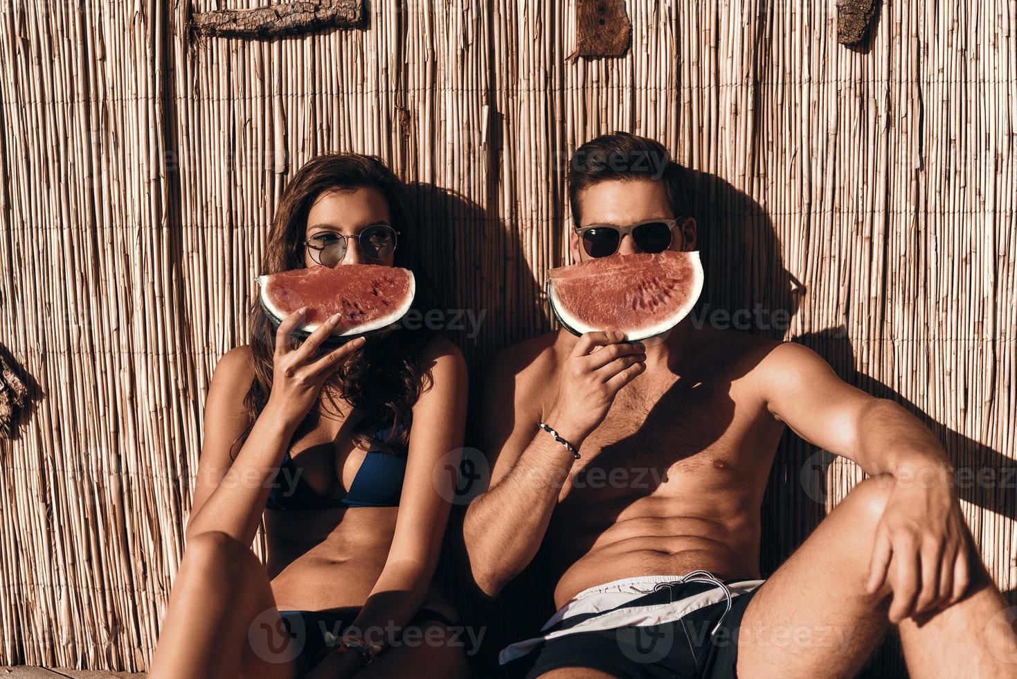 succoso e dolce. bellissimo giovane coppia copertura un' metà di loro facce con un' fetta di anguria mentre seduta all'aperto foto