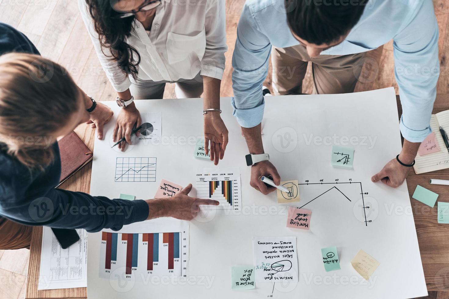 andando al di sopra di particolari. vicino su superiore Visualizza di giovane fiducioso attività commerciale persone Lavorando insieme mentre uomo scrittura su planimetria nel il ufficio foto