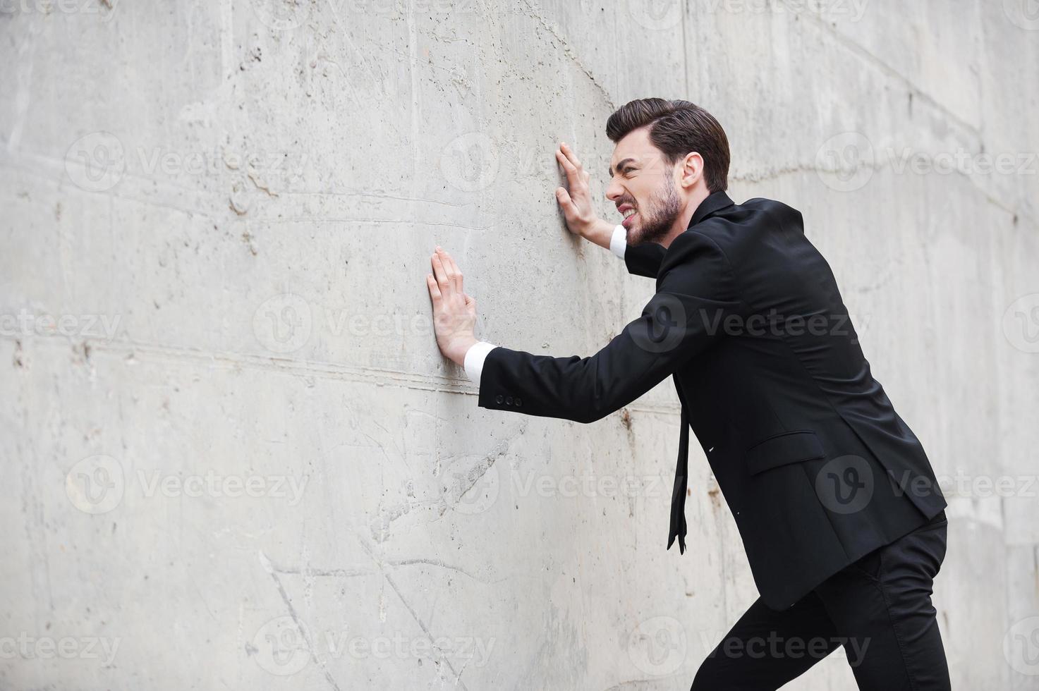 provando per venire su di fatica. frustrato giovane uomo nel vestito formale spingendo il parete mentre in piedi all'aperto foto