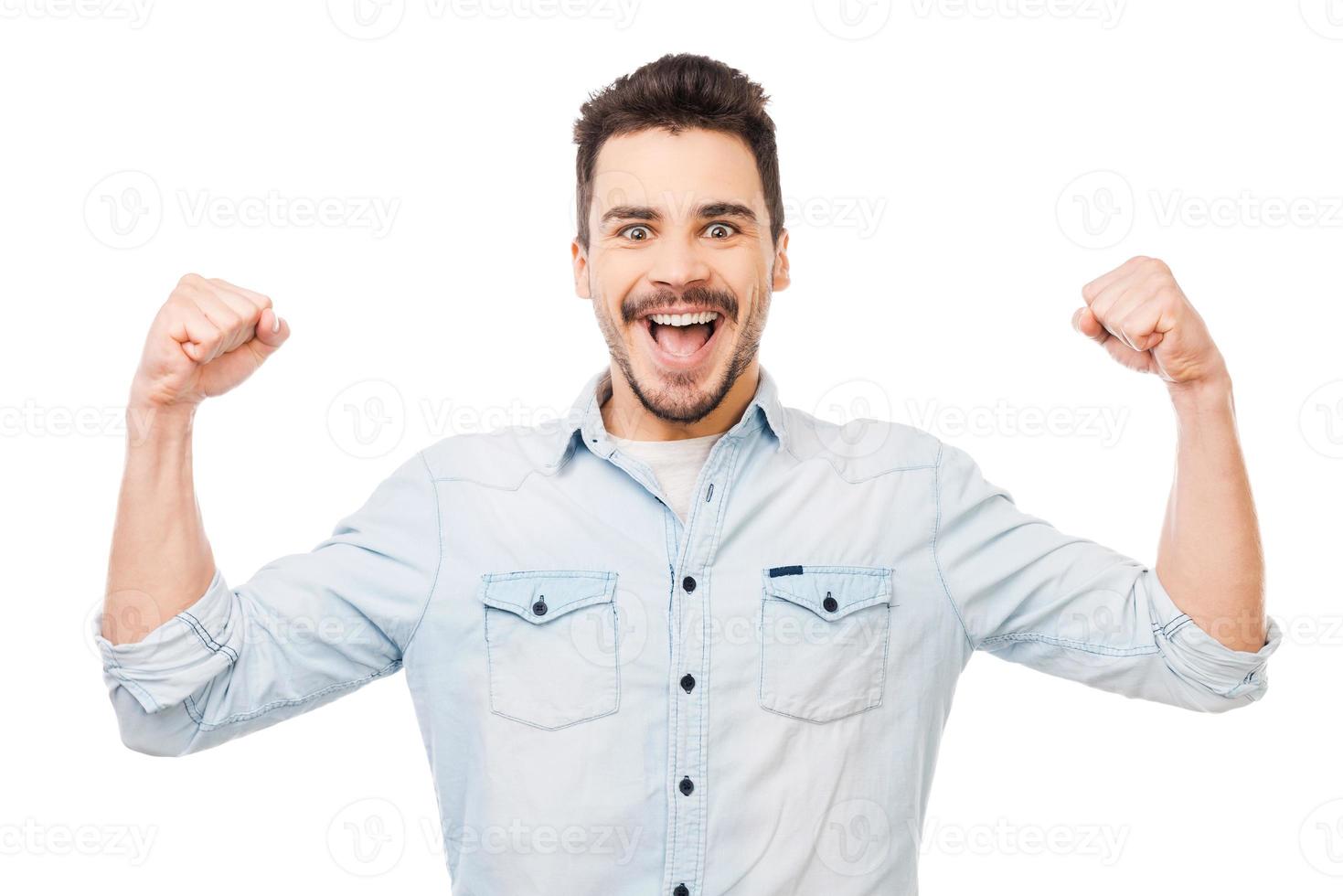 scatenato divertimento. contento giovane uomo nel camicia Esprimere a gesti e sorridente mentre in piedi contro bianca sfondo foto