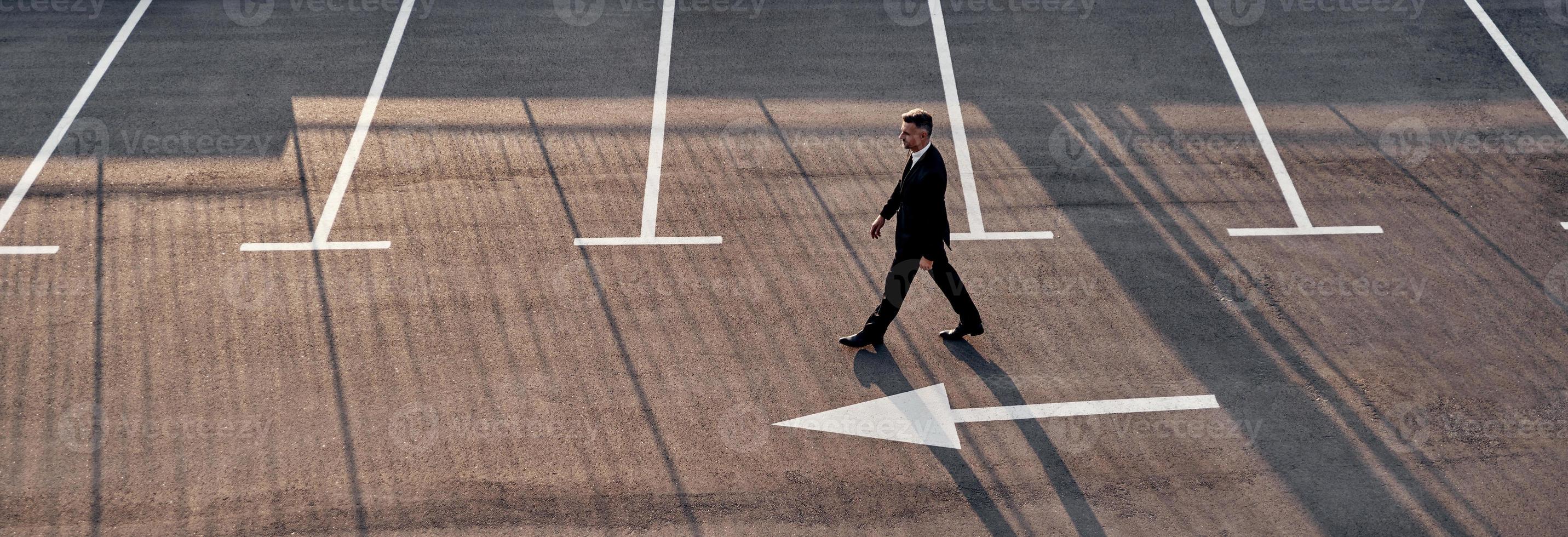 superiore Visualizza di uomo nel vestito formale in movimento inoltrare con freccia cartello su il strada foto