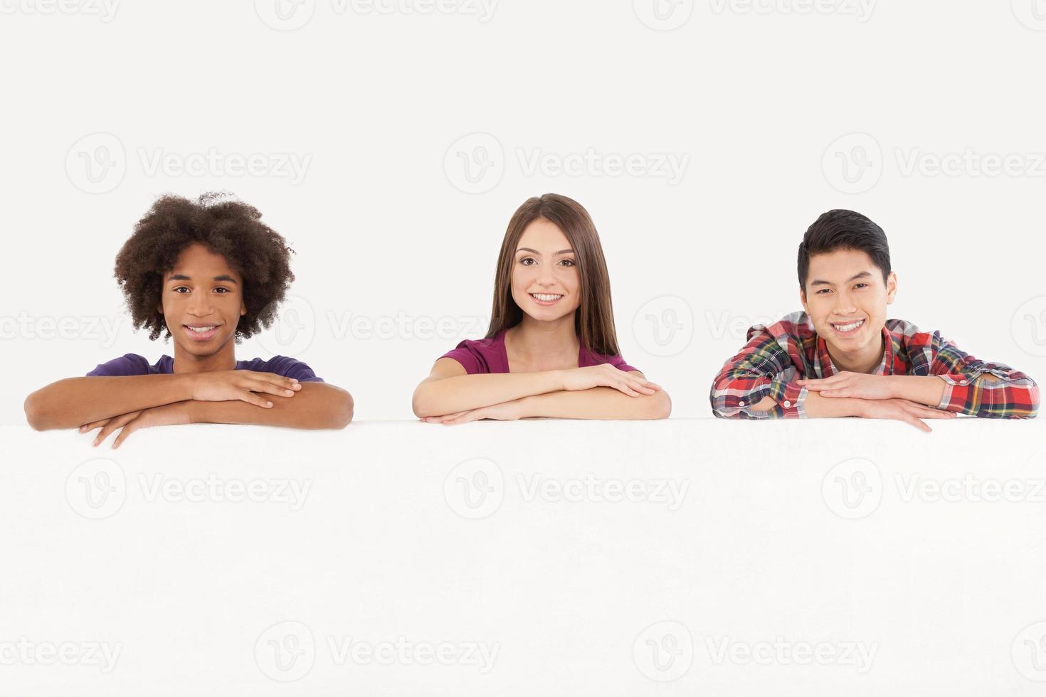 amici con copia spazio. allegro giovane multietnico persone pendente a copia spazio e sorridente a telecamera mentre isolato su bianca foto