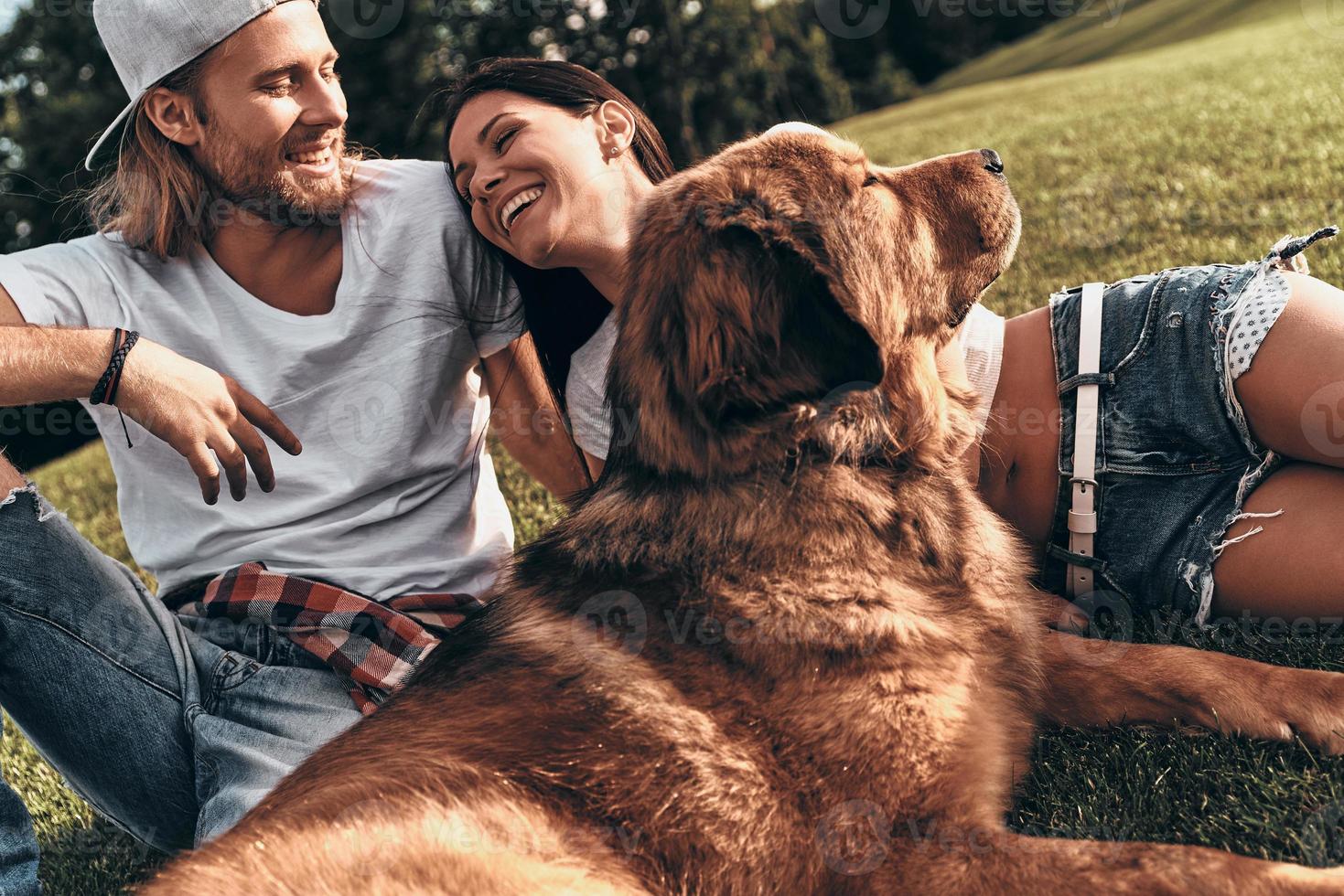 Niente altro ma amore. giovane moderno coppia dire bugie su il erba con loro cane mentre la spesa gratuito tempo nel il parco foto