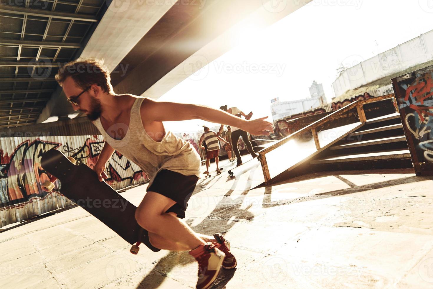 pronto per rendere sforzo. giovane moderno uomini andare con lo skateboard mentre sospeso su con il suo amici a il pattinare parco all'aperto foto