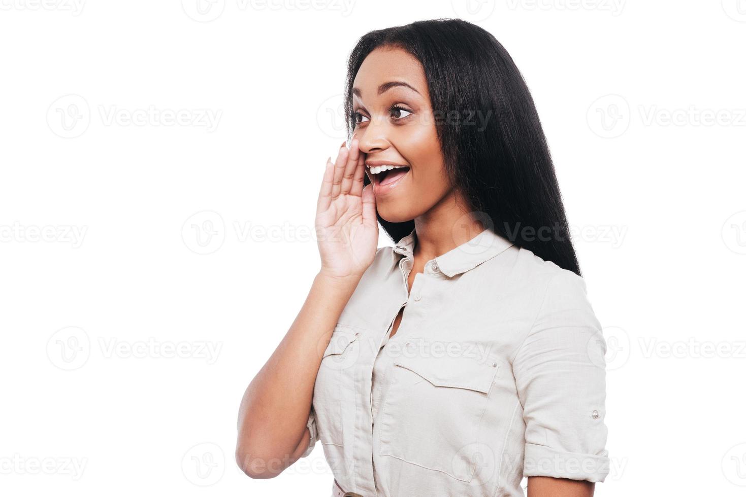 condivisione bene notizia. lato Visualizza di allegro giovane africano donna Tenere mani in giro bocca e urlando mentre in piedi contro bianca sfondo foto