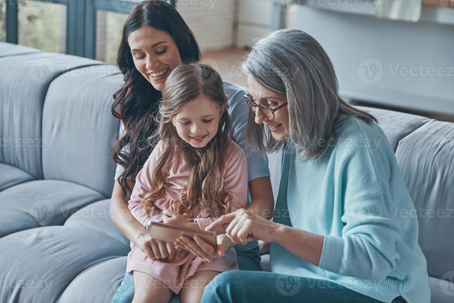 contento poco ragazza l'esame inteligente Telefono mentre la spesa tempo con madre e nonna a casa foto