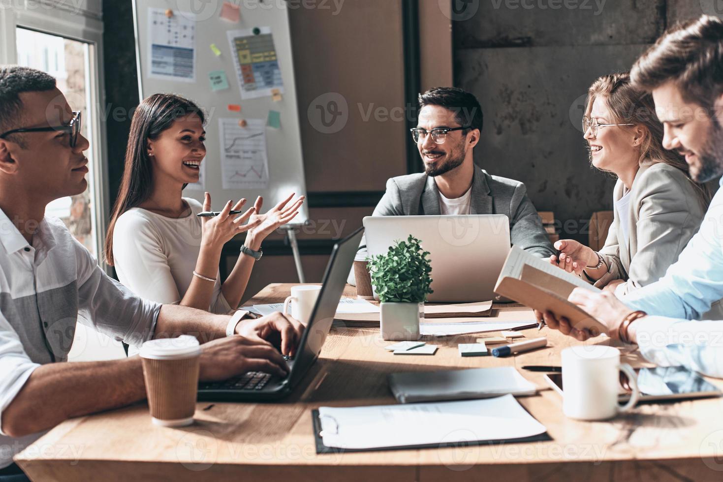 Lavorando insieme. gruppo di giovane moderno persone nel inteligente casuale indossare discutere attività commerciale e sorridente mentre seduta nel il creativo ufficio foto