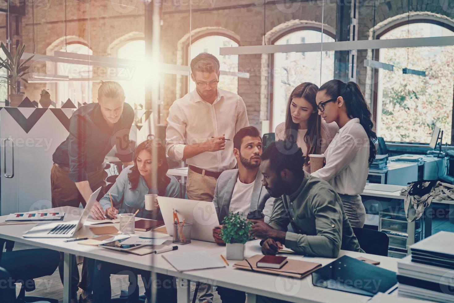 gruppo di giovane moderno persone nel inteligente casuale indossare comunicare e utilizzando moderno tecnologie mentre Lavorando nel il ufficio foto