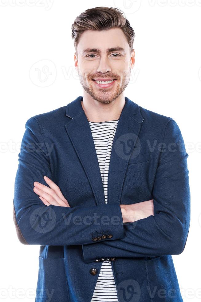 fiducioso giovane uomo. bello giovane uomo conservazione braccia attraversato e sorridente mentre in piedi contro bianca sfondo foto