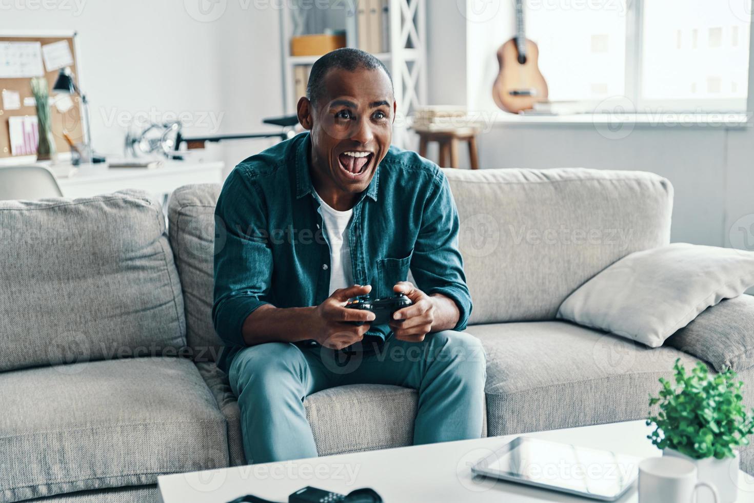 bello giovane africano uomo giocando video gioco e sorridente mentre seduta in casa foto