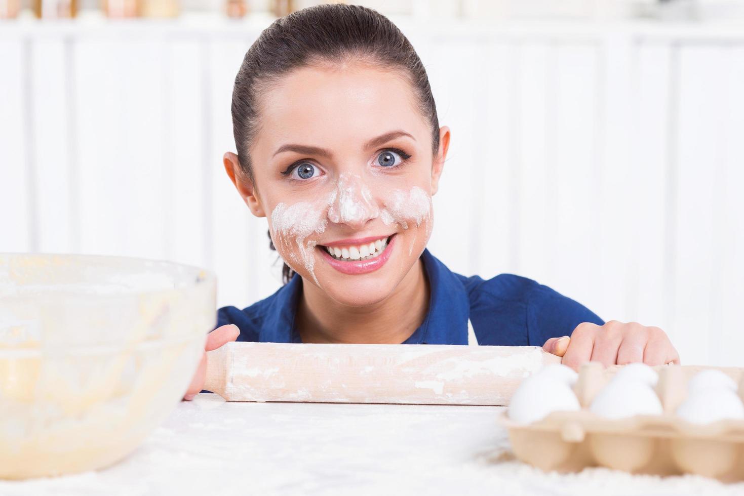 disordinato cucinando. giocoso giovane donna con gusto su viso Tenere rotolamento perno e guardare su di il cucina tavolo foto