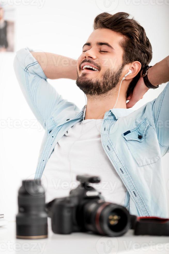 tempo per un' minuto rompere. allegro giovane uomo nel cuffie Tenere testa nel mani e sorridente mentre seduta a il suo Lavorando posto foto