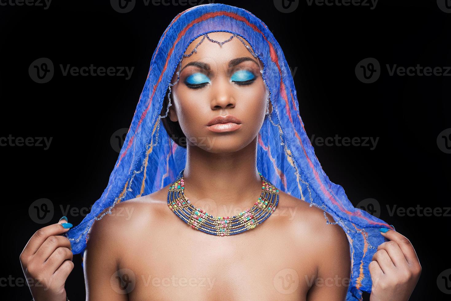 pure bellissimo per essere VERO. bellissimo africano donna copertura testa di sciarpa e conservazione occhi chiuso mentre in piedi contro nero sfondo foto