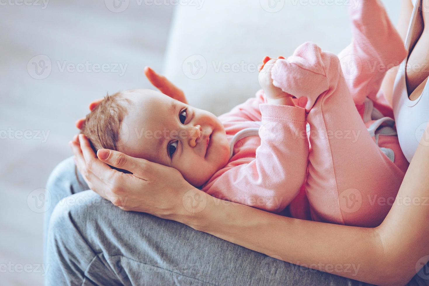 poco tesoro. vicino su lato Visualizza parte di giovane donna Tenere sorridente bambino ragazza su sua ginocchia mentre seduta su il divano foto