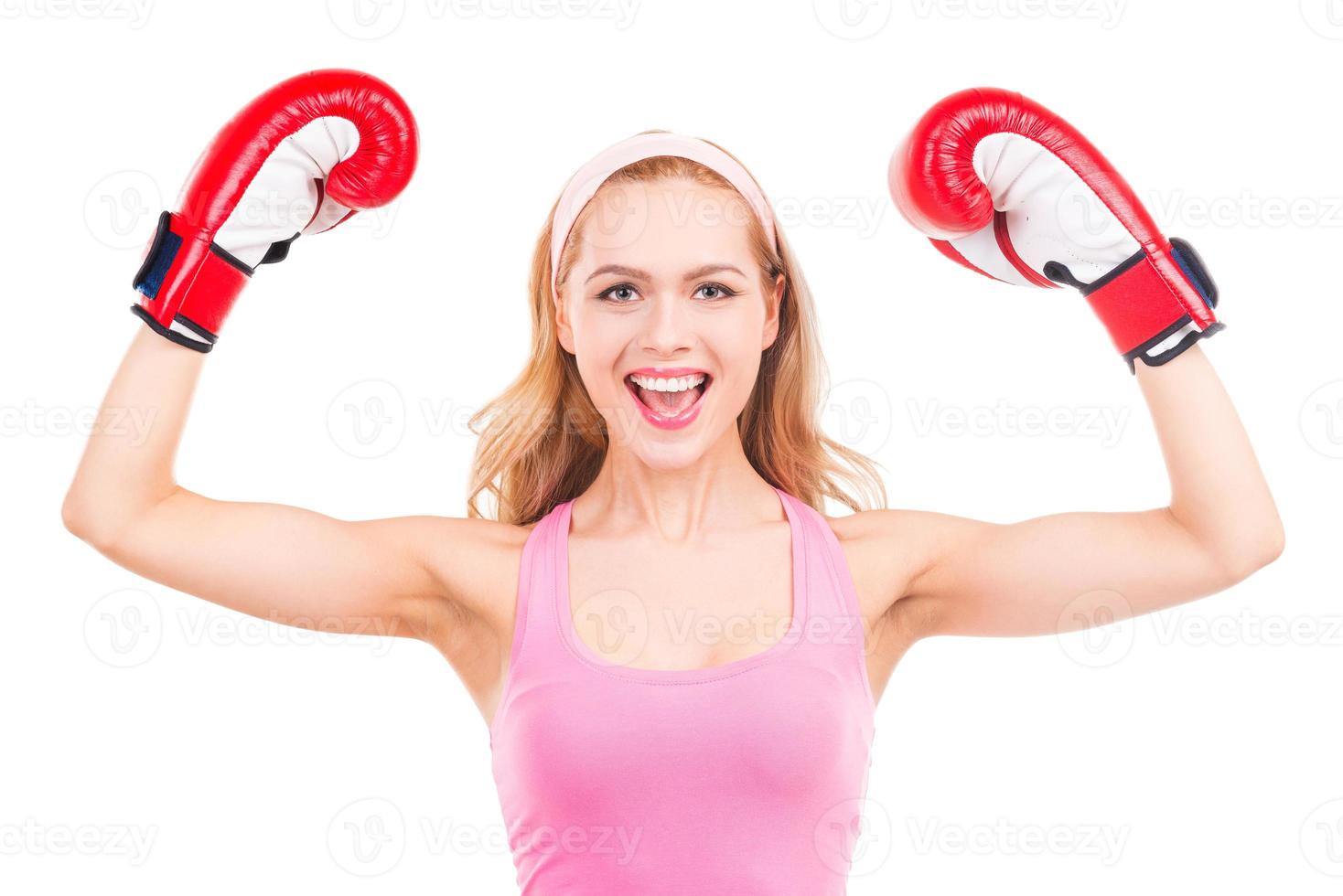 bellissimo vincitore. bellissimo biondo capelli donna nel rosa gli sport capi di abbigliamento e boxe guanti Esprimere a gesti e sorridente mentre in piedi isolato su bianca sfondo foto