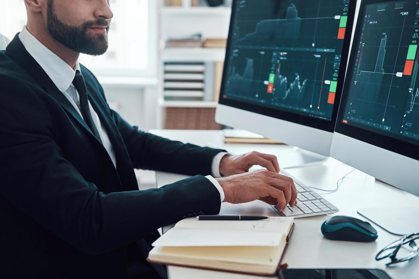 vicino su di giovane uomo nel camicia e cravatta digitando qualcosa utilizzando computer mentre Lavorando nel il ufficio foto