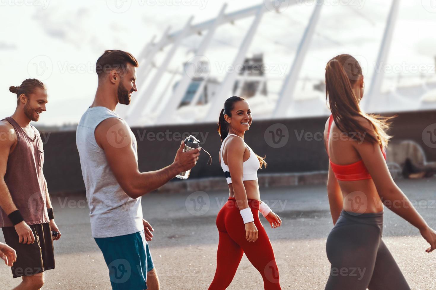 gruppo di giovane persone nel gli sport capi di abbigliamento a piedi mentre rilassante dopo esercizio all'aperto foto