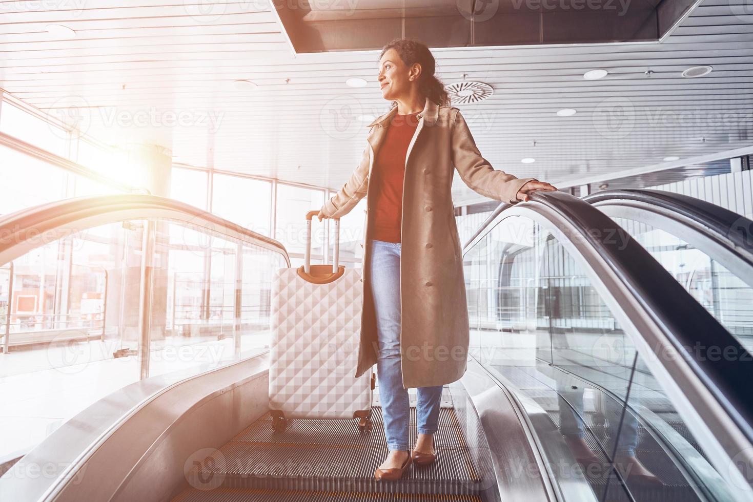 bellissimo maturo donna sorridente e guardare lontano mentre in movimento di scala mobile nel aeroporto terminale foto