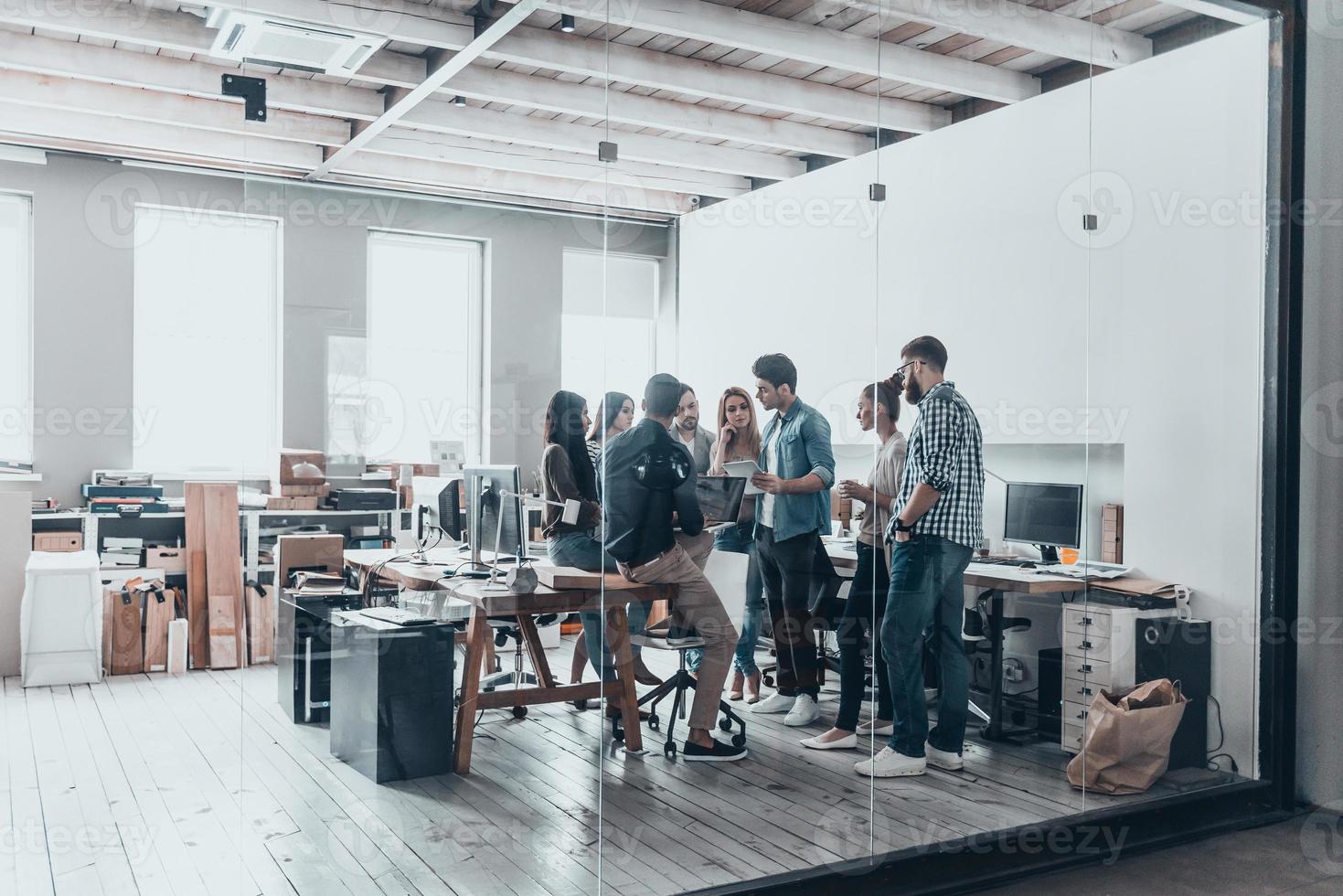 lavoro di squadra è un' chiave per successo. pieno lunghezza di giovane moderno persone nel inteligente casuale indossare discutere attività commerciale mentre in piedi dietro a il bicchiere parete nel il creativo ufficio foto