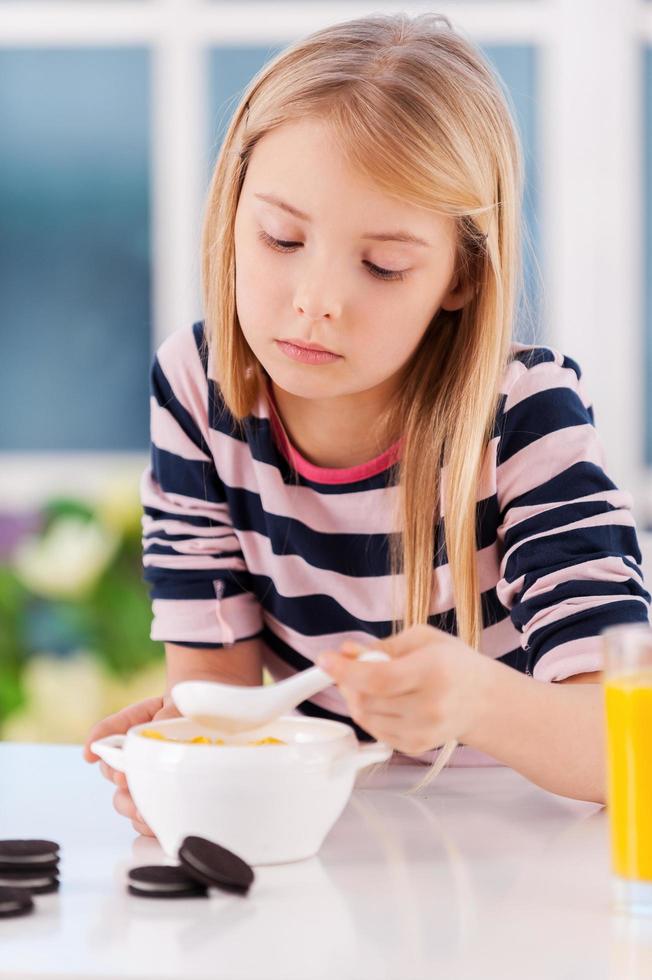 io am non Affamato. triste poco ragazza mangiare qualcosa a partire dal il piatto mentre seduta a il tavolo foto