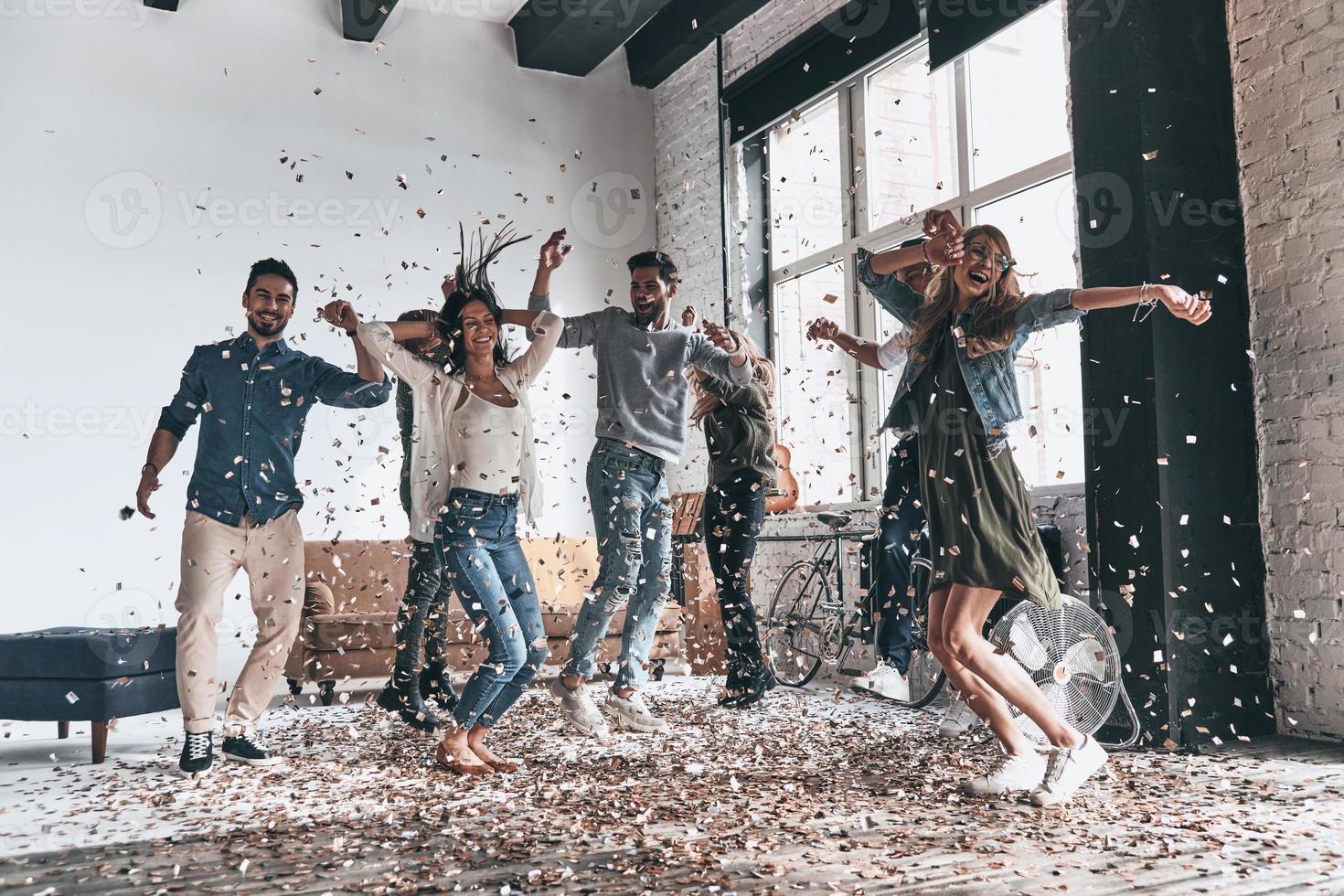 godendo spensierato volta. pieno lunghezza di contento giovane persone danza mentre avendo un' festa con coriandoli volante ovunque foto