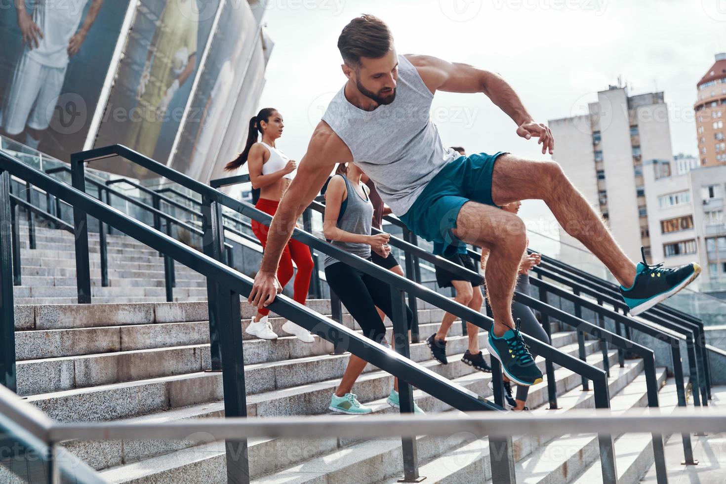 giovane uomo nel gli sport capi di abbigliamento salto mentre esercizio con il suo amici su il le scale all'aperto foto