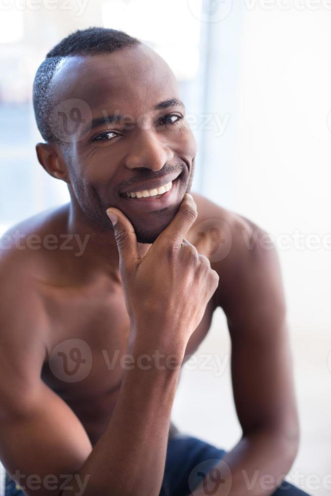 A petto nudo nero uomo. A petto nudo africano uomo Tenere mano su mento e sorridente a telecamera foto