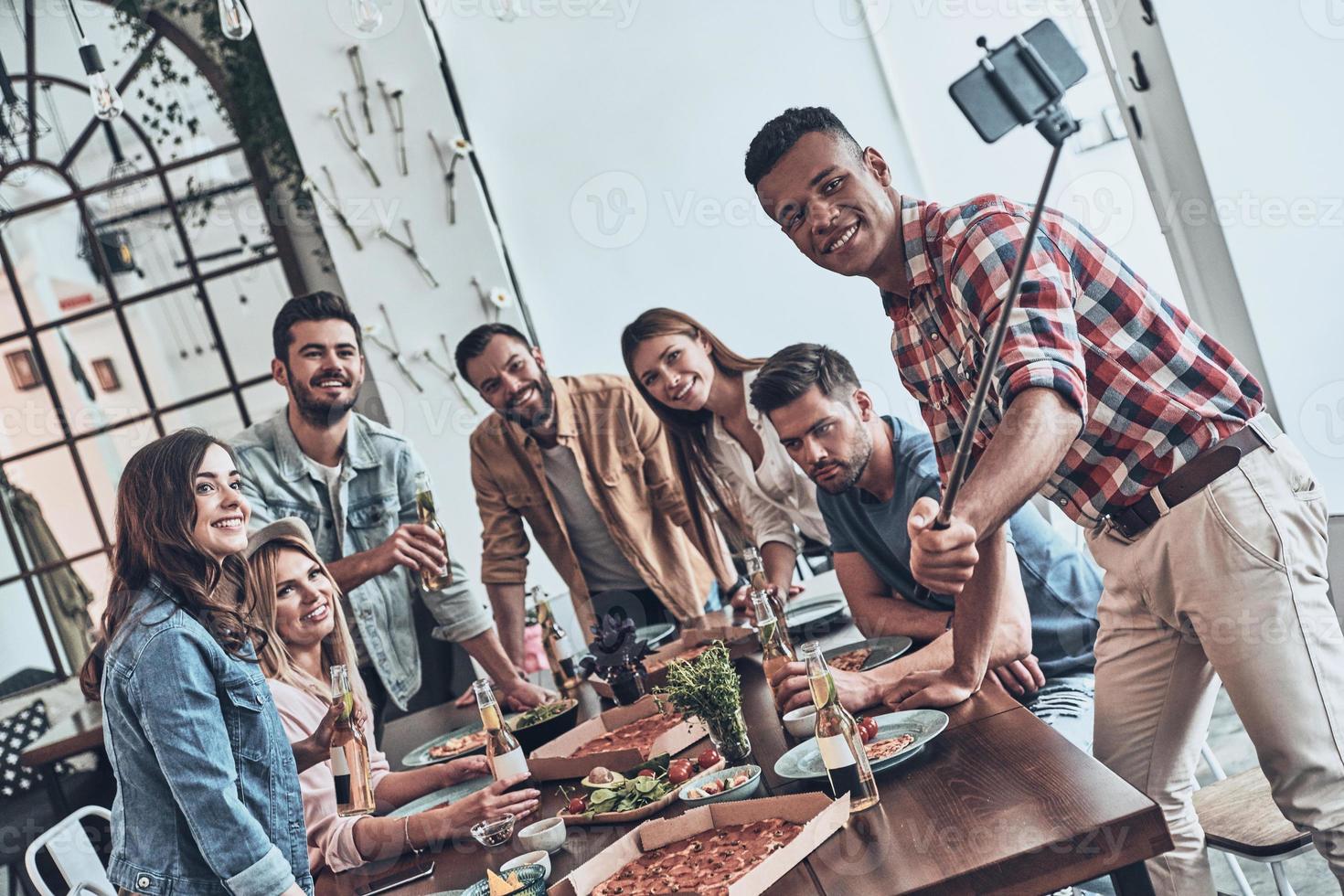 gruppo di giovane moderno persone assunzione autoscatto utilizzando inteligente Telefono mentre essi avendo un' cena festa foto