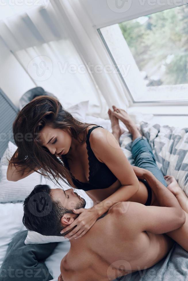 godendo tempo insieme. superiore Visualizza di bellissimo giovane semivestito donna seduta su il superiore di sua fidanzato mentre la spesa tempo nel il letto foto