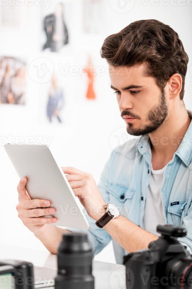 concentrato su opera. bello giovane uomo Lavorando su digitale tavoletta mentre seduta a il suo Lavorando posto foto