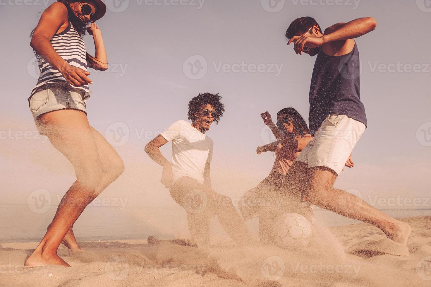 spiaggia palla divertimento. gruppo di allegro giovane persone giocando con calcio palla su il spiaggia foto