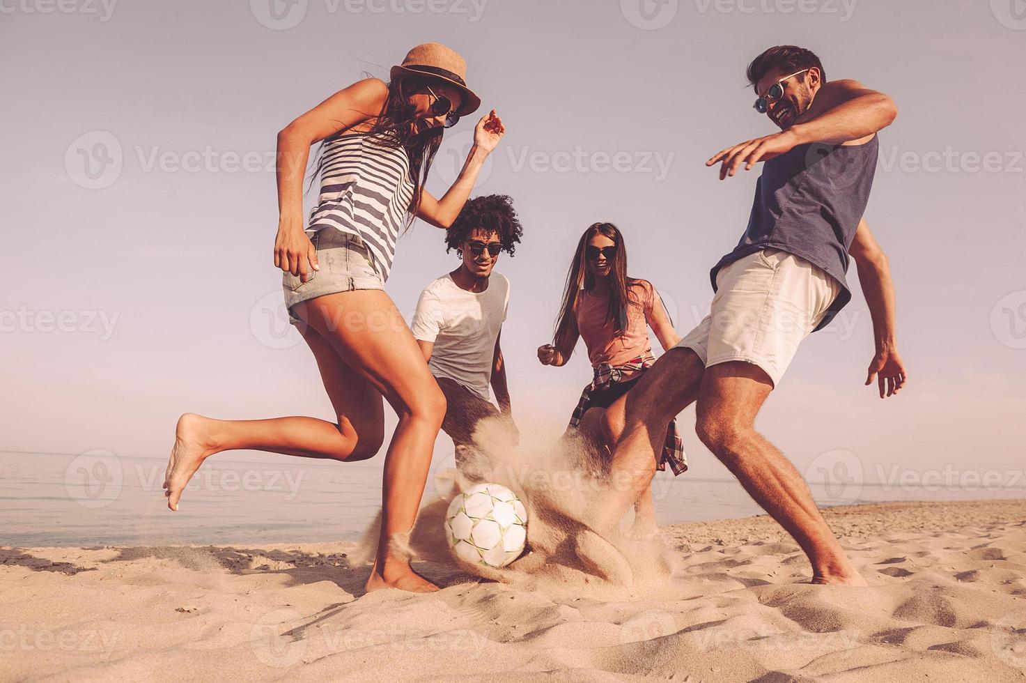 divertimento tempo con gli amici. gruppo di allegro giovane persone giocando con calcio palla su il spiaggia foto