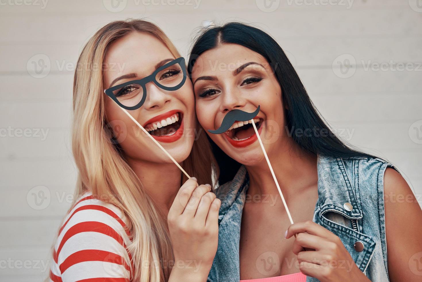 spensierato divertimento. Due allegro giovane donne fabbricazione facce mentre in piedi all'aperto foto