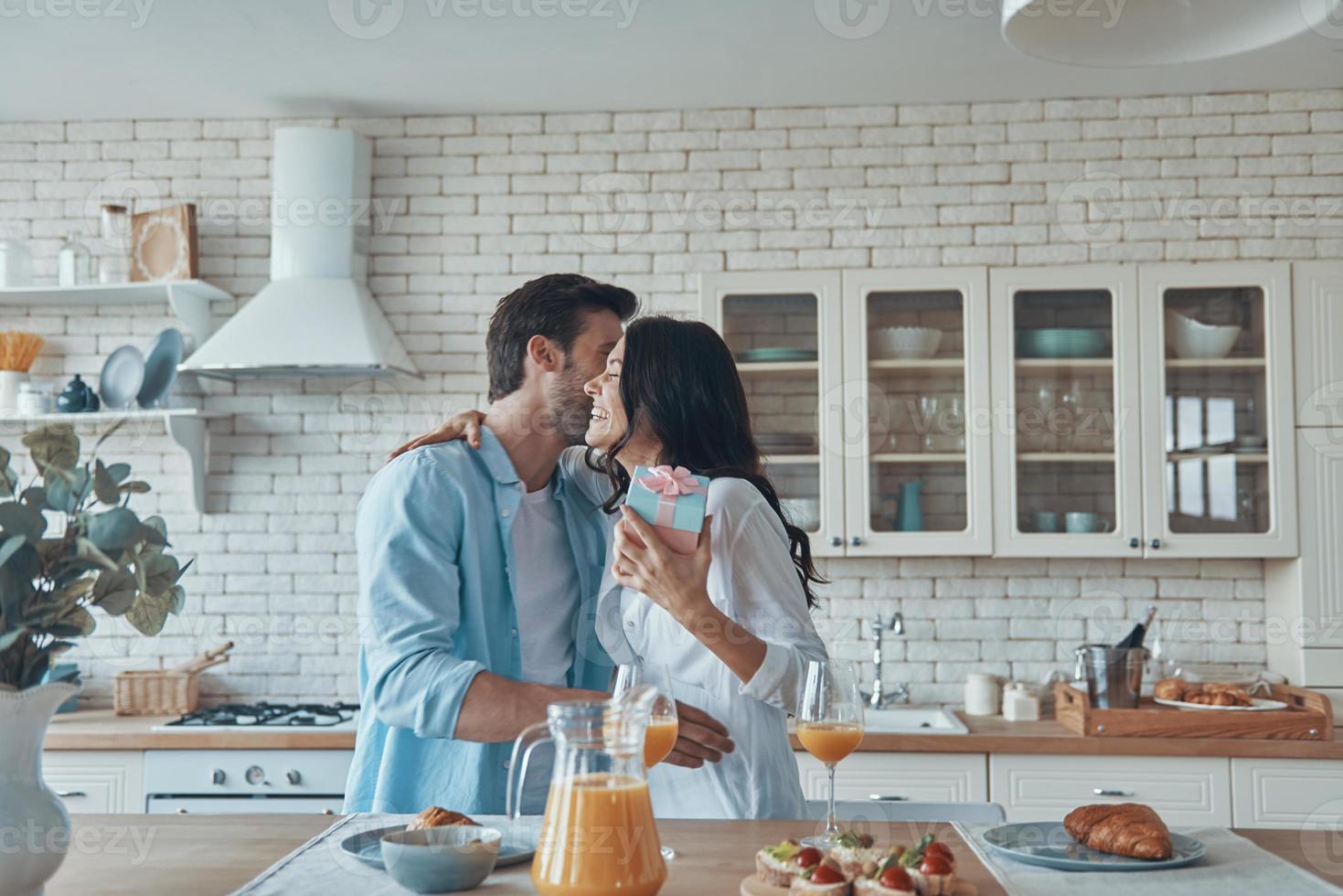 giovane uomo dando un' regalo scatola per il suo fidanzata mentre avendo prima colazione a il domestico cucina insieme foto