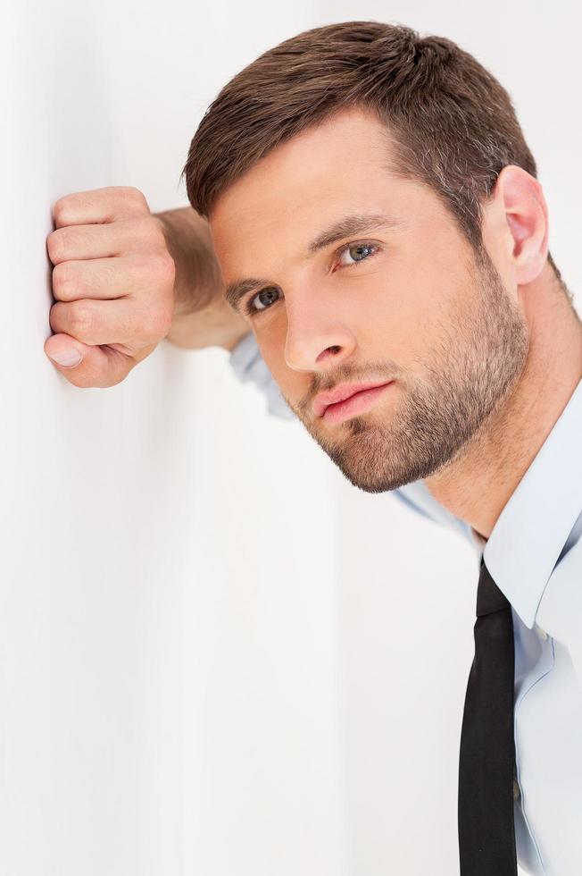 fiducioso e ispirato. bello giovane uomo nel camicia e cravatta pendente a il parete e guardare lontano foto