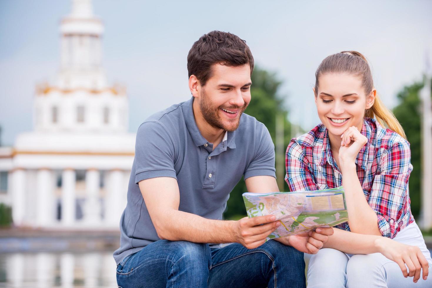 la scelta il posto per andare. contento giovane turista coppia seduta vicino bellissimo edificio e l'esame carta geografica insieme foto