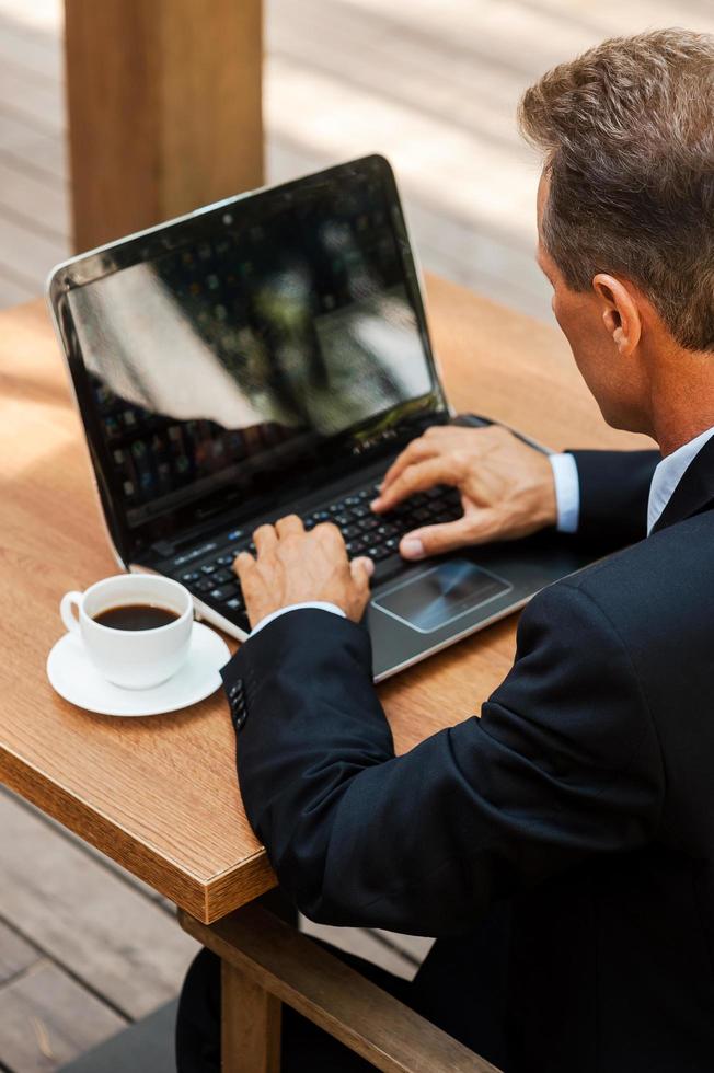 uomo d'affari Lavorando all'aperto. superiore Visualizza di maturo uomo nel vestito formale Lavorando su il computer portatile mentre seduta a il tavolo all'aperto foto