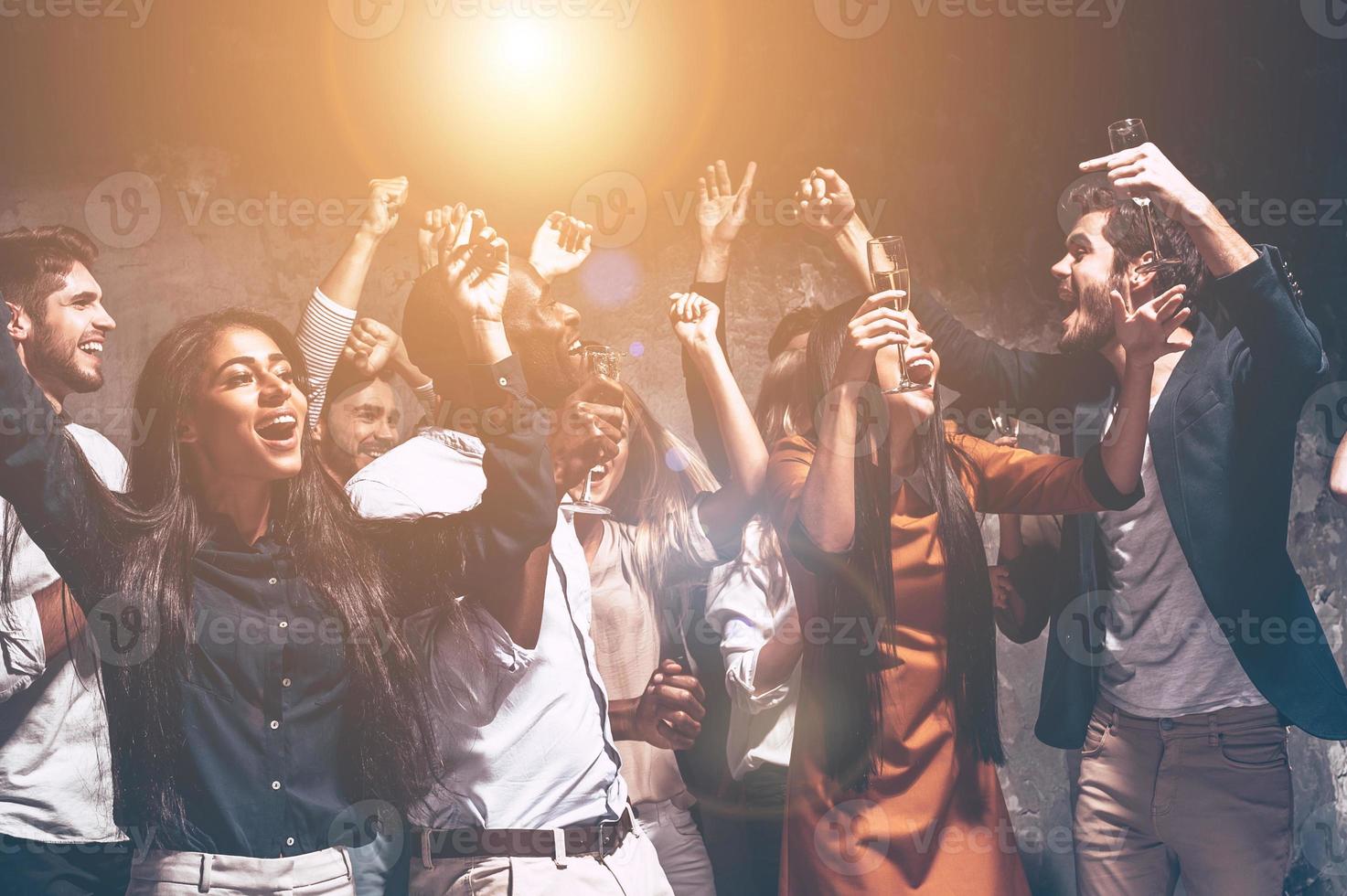 festa tutti notte lungo. gruppo di bellissimo giovane persone danza con Champagne flauti e guardare contento foto