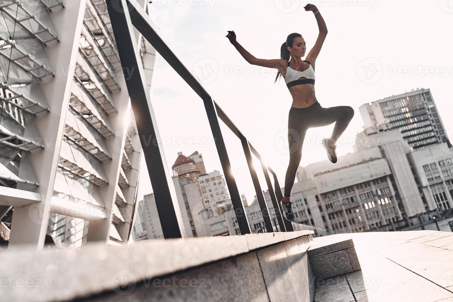 mai fermare pieno lunghezza di moderno giovane donna nel gli sport capi di abbigliamento salto mentre esercizio all'aperto foto