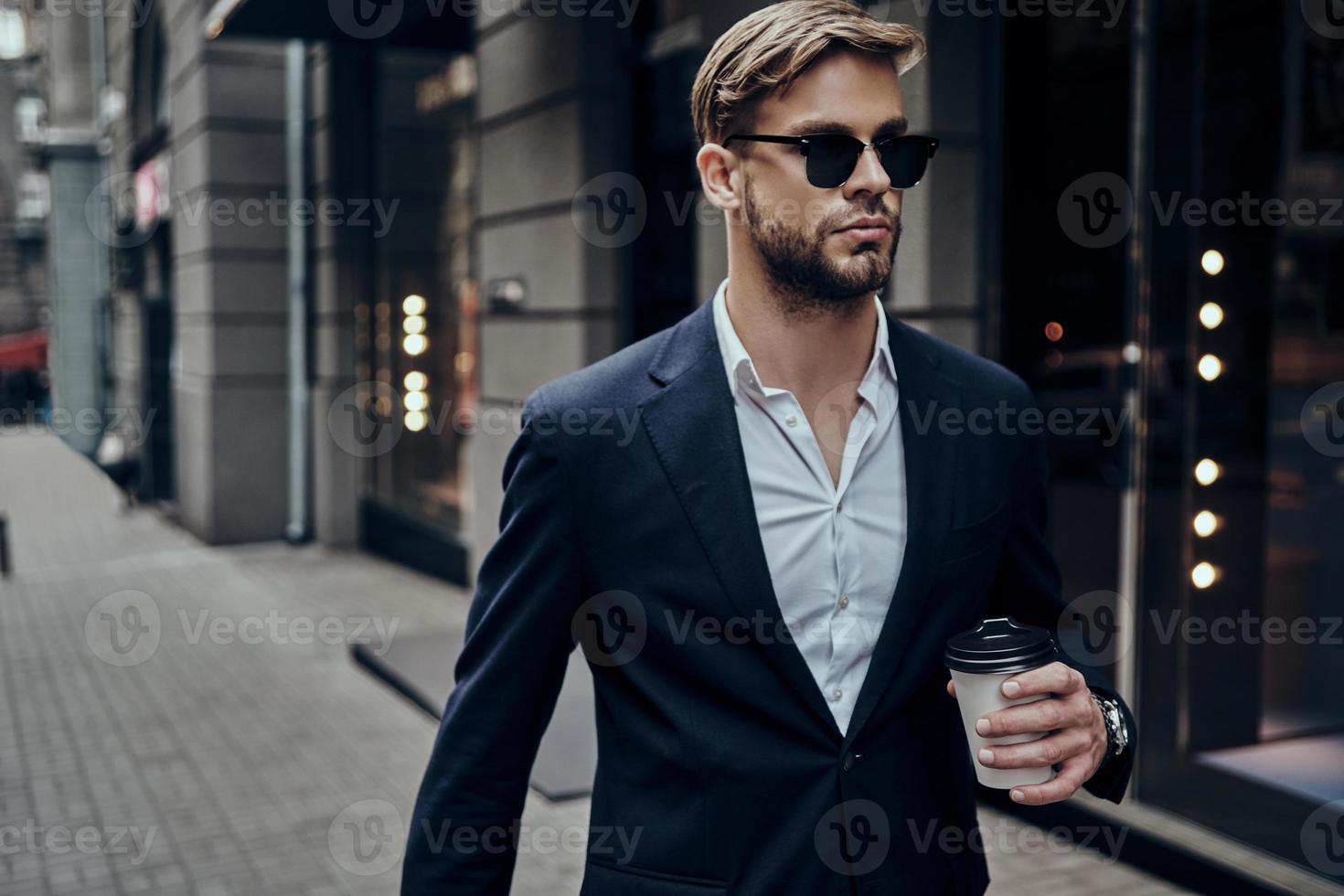 Perfetto uomo d'affari. bello giovane uomo nel inteligente casuale indossare trasporto monouso tazza mentre a piedi attraverso il città strada foto