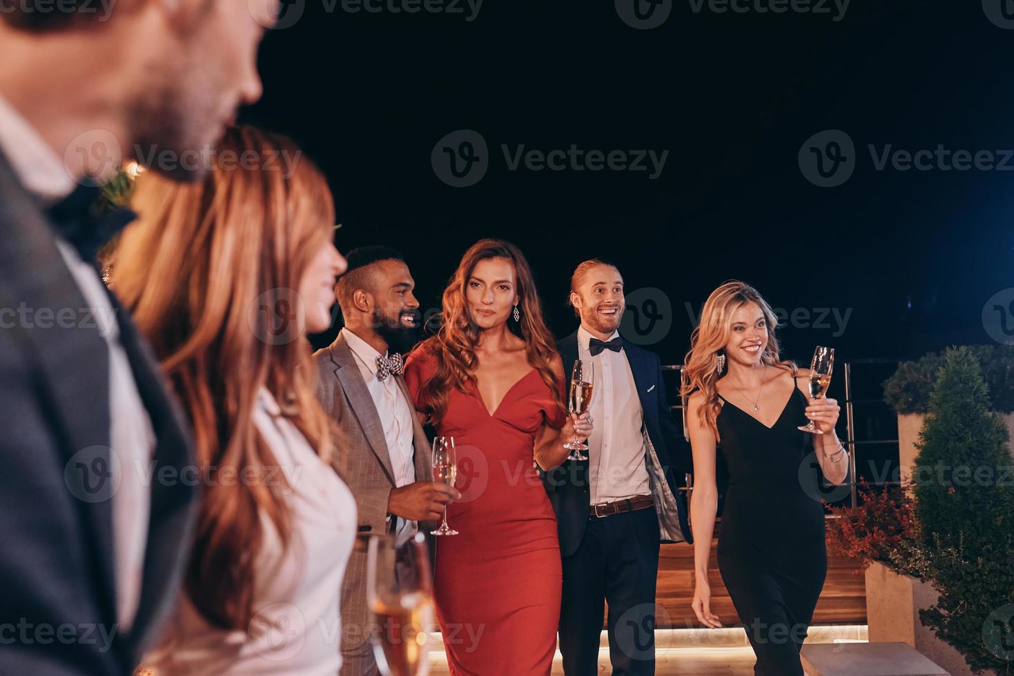gruppo di persone nel vestito formale comunicare e sorridente mentre la spesa tempo su lusso festa foto