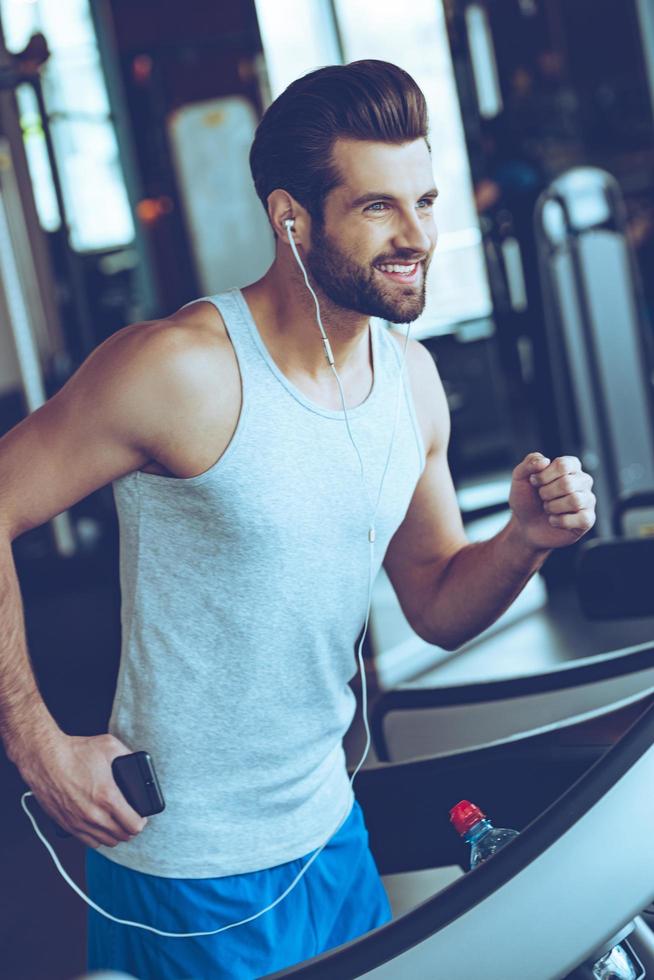 cinque miglia con piacere. allegro giovane bello uomo nel cuffie guardare lontano con Sorridi mentre in esecuzione su routine a Palestra foto