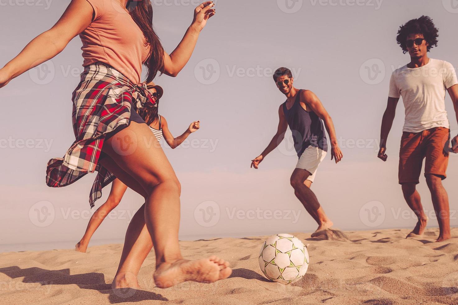 spiaggia divertimento. gruppo di allegro giovane persone giocando con calcio palla su il spiaggia foto