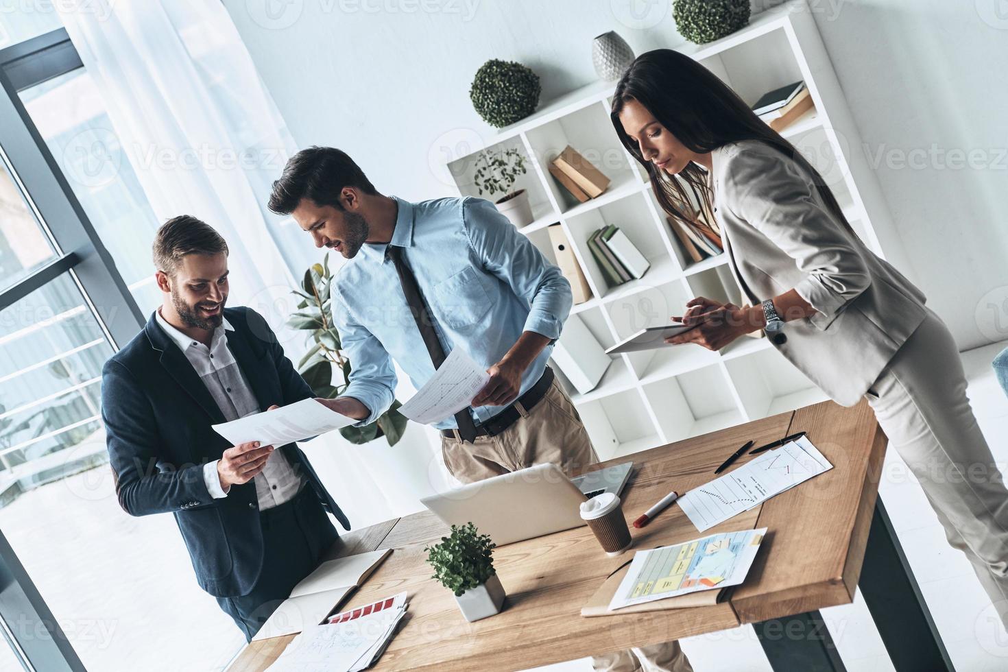 Lavorando giorno. superiore Visualizza di giovane moderno persone nel inteligente casuale indossare discutere attività commerciale mentre in piedi nel il creativo ufficio foto