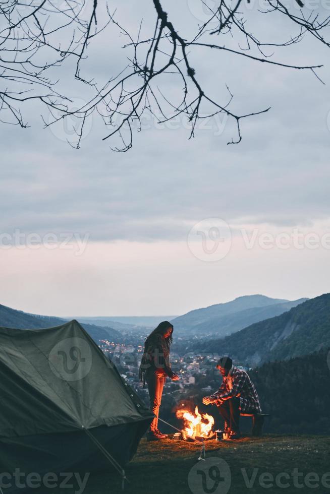 migliore modo per mantenere voi caldo. bellissimo giovane coppia riscaldamento su di il fuoco di bivacco mentre campeggio nel il montagne foto