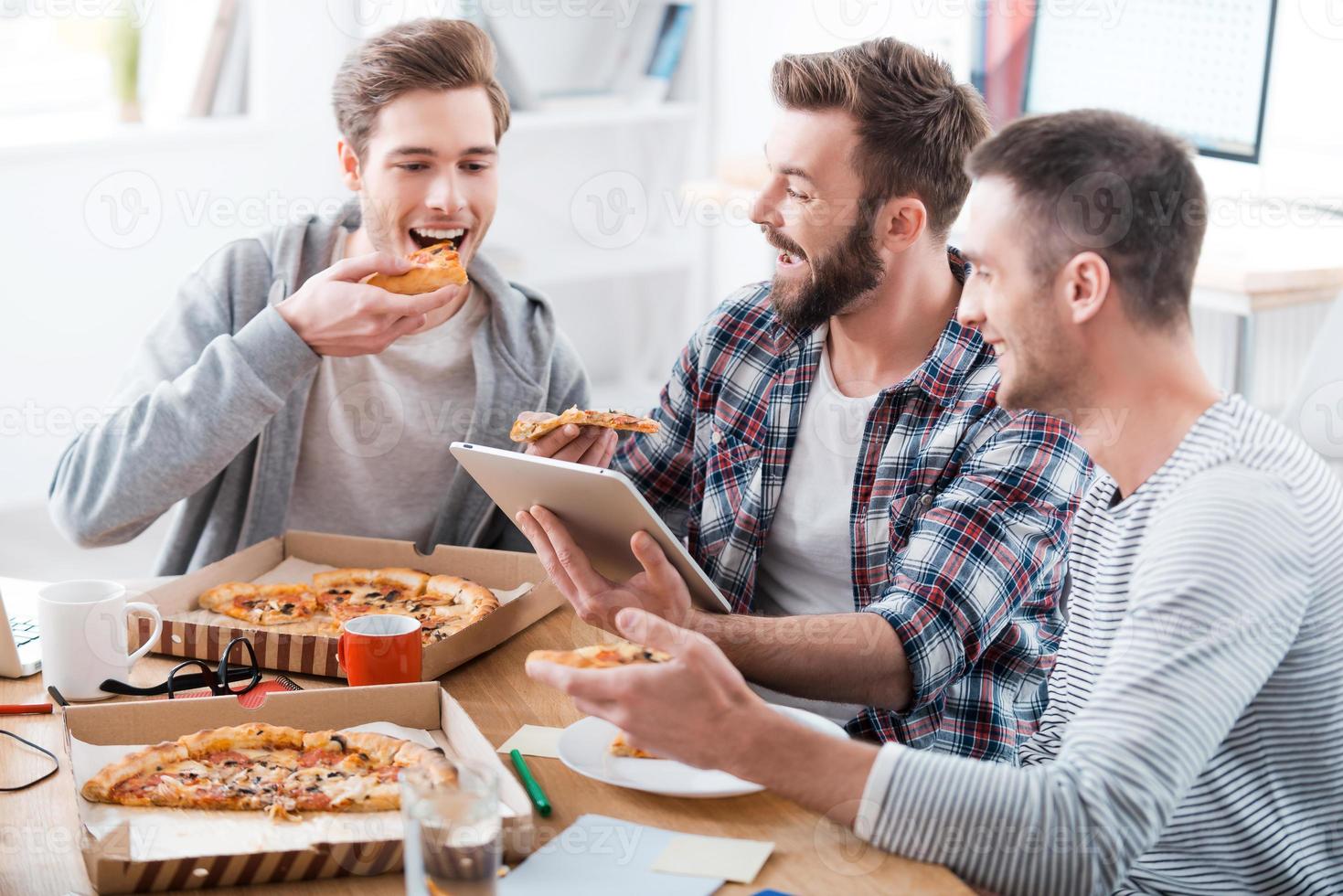 Pizza tempo tre giovane allegro uomini mangiare Pizza insieme mentre seduta nel il ufficio foto